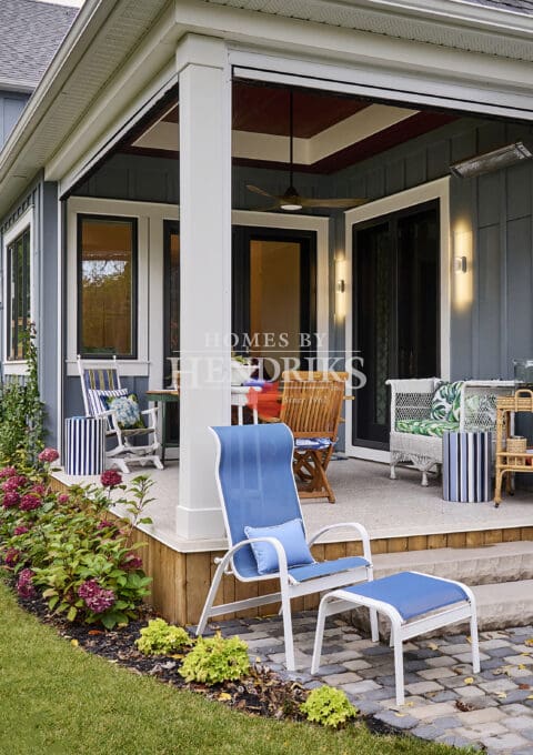 Exterior view of a dining space featuring teak outdoor furniture and an exterior heater, set against a backdrop of grey Hardie board and batten siding, creating a cozy and stylish outdoor atmosphere.