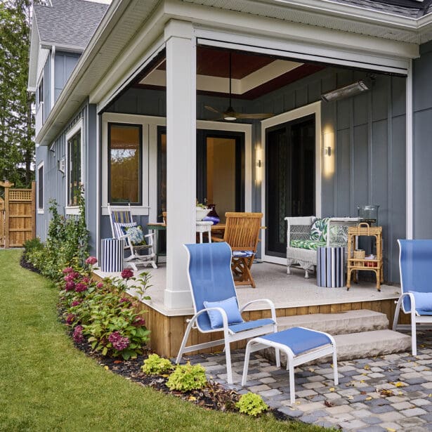 Exterior view of a dining space featuring teak outdoor furniture and an exterior heater, set against a backdrop of grey Hardie board and batten siding, creating a cozy and stylish outdoor atmosphere.