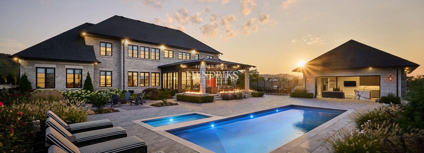 Stunning custom home with a luxurious stone exterior featuring limestone accents, surrounded by lush landscaping and a beautifully designed pool, showcasing an elegant and timeless architectural style.