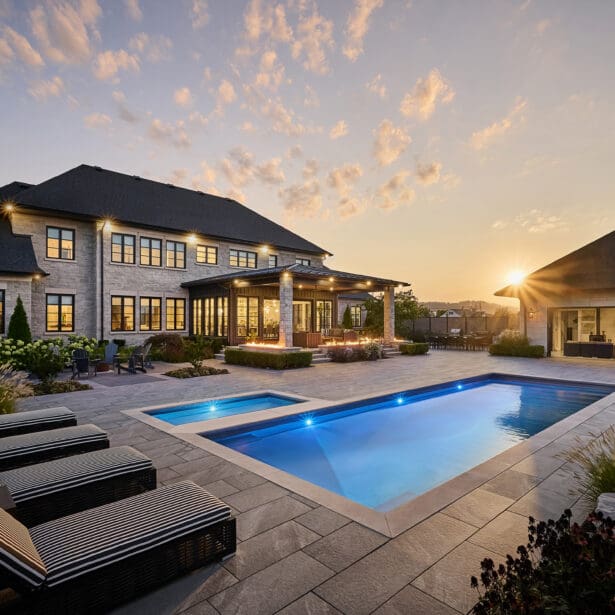 Stunning custom home with a luxurious stone exterior featuring limestone accents, surrounded by lush landscaping and a beautifully designed pool, showcasing an elegant and timeless architectural style.